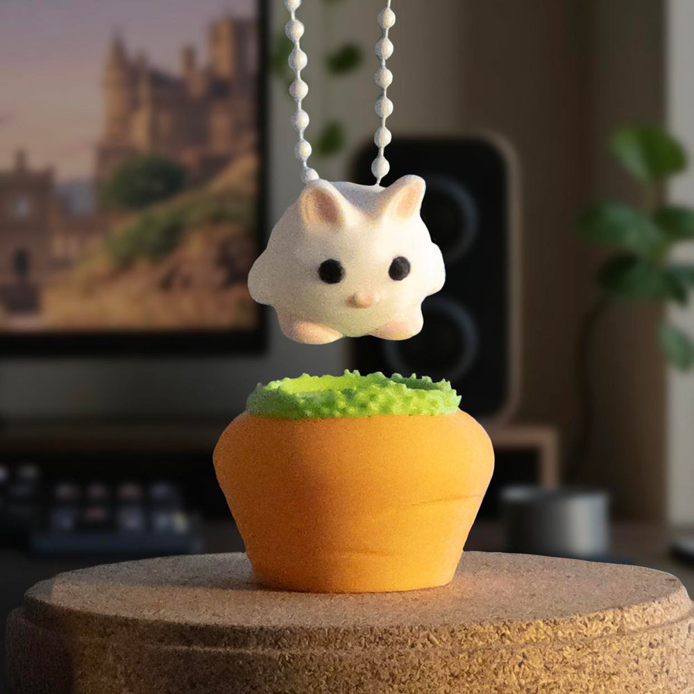 A cute white bunny charm being held by a keychain above a carrot-shaped pot with a grassy top, ready to be placed back.