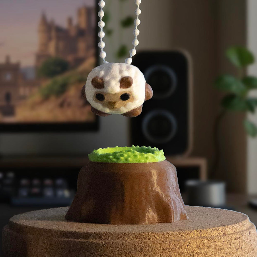 A fluffy sheep charm being held by a keychain above a grassy tree stump display, ready to be placed back on its stand.